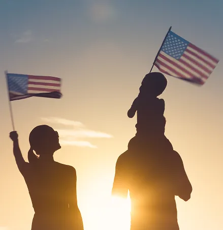 Family raising US flag facing sunset
